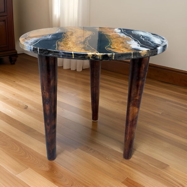 Elegant round table with a high-gloss top featuring rich blue and gold marbling effects that create a luxurious look. The Artisan Centerpiece table stands on three dark stained wooden legs that taper gracefully, complementing the sophisticated top. Set in a room with hardwood flooring and natural light, this table blends modern design with classic elegance, ideal for enhancing any contemporary home setting.
